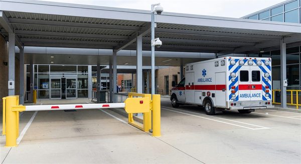 Hospital ambulance bay with controlled access gate, security camera, and EMS vehicle in position