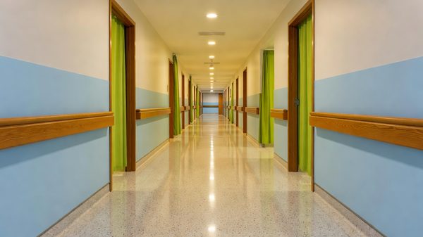 Hospital corridor with handrails and doorways leading to patient rooms under even lighting