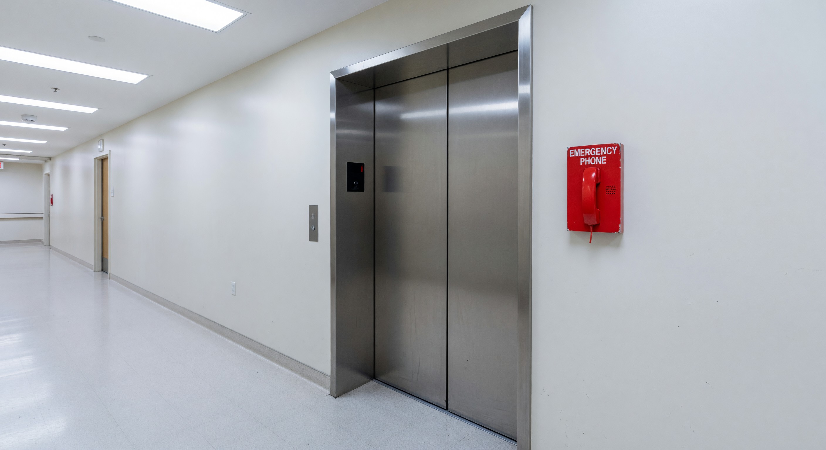 Hospital elevator lobby with wide bariatric elevator and emergency phone panel visible