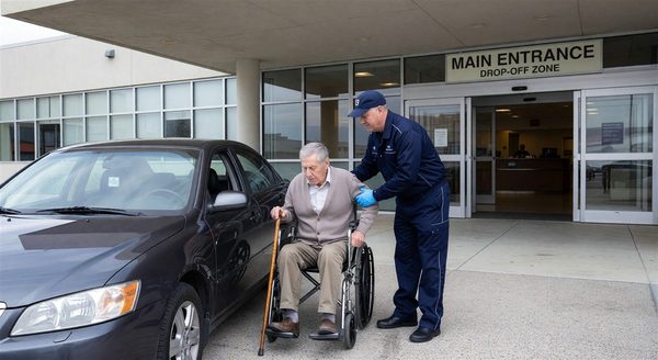 Hospital valet attendant assisting an elderly patient at a main entrance drop-off zone