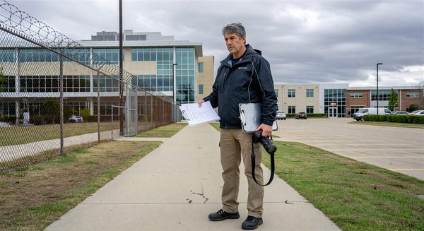 Security consultant conducting hospital campus perimeter assessment with clipboard and camera